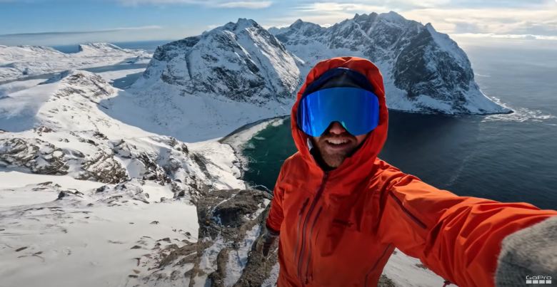 man in an orange jacket taking a selfie in a snowy landscape