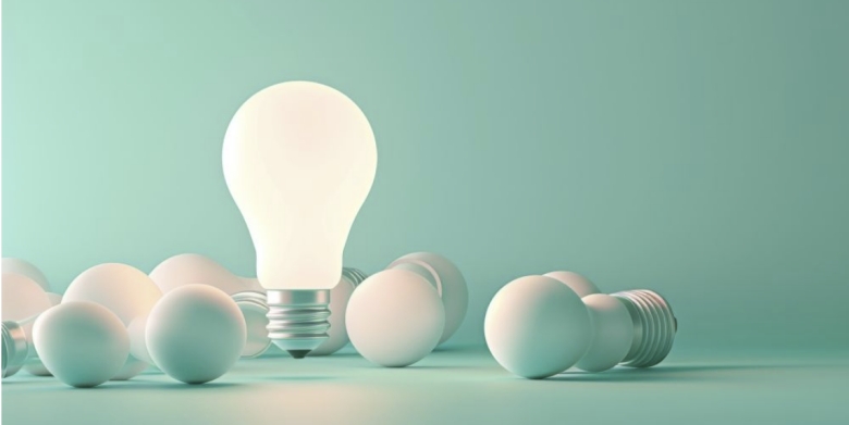 Glowing light bulb standing amid several unlit bulbs on a teal background