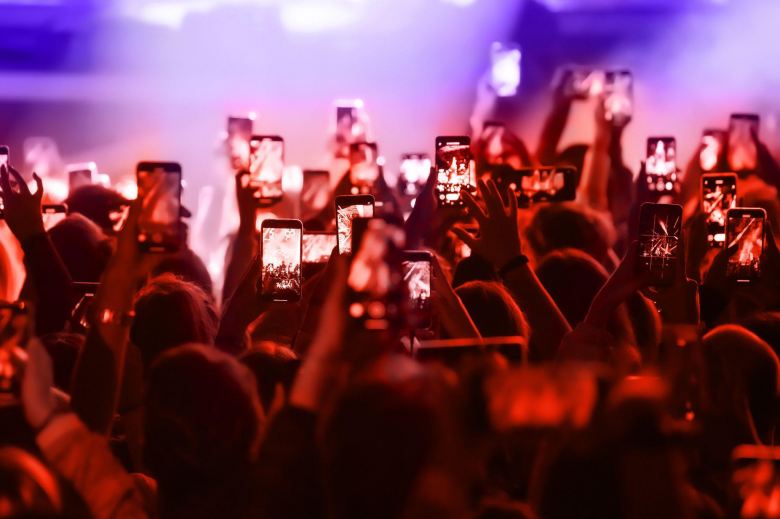 people in a concert holding their phone up to record a video of the stage