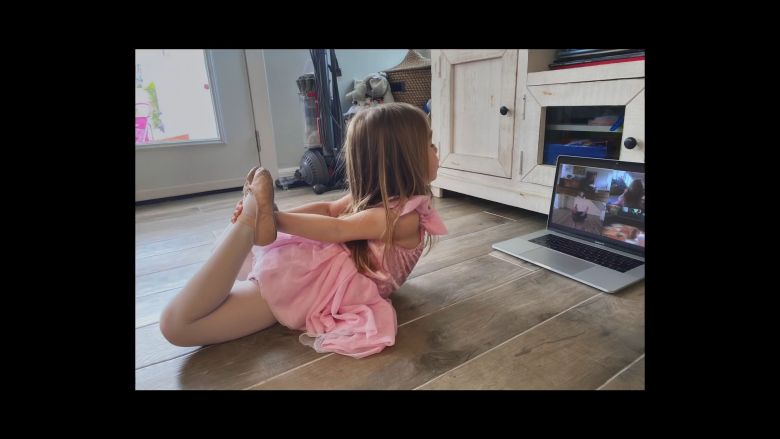 little girl performing a ballerina pose with a macbook in front of her