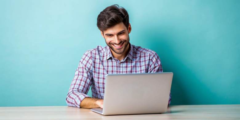 man smiling sitting at a desk and working on a laptop