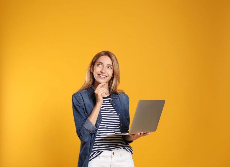 young blonde woman smiling and holding a laptop in a yellow background