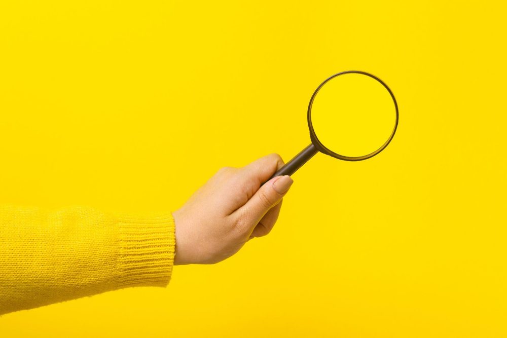 Hand holding a magnifying glass against a yellow background