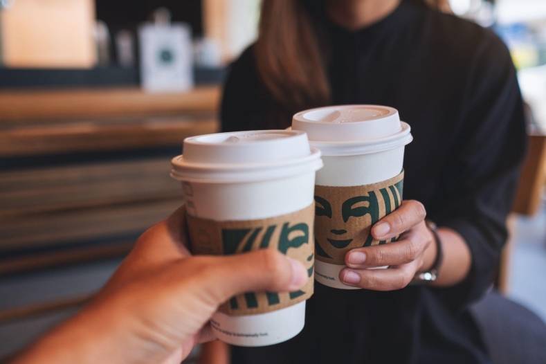 Two people clinking Starbucks coffee cups in a cozy setting