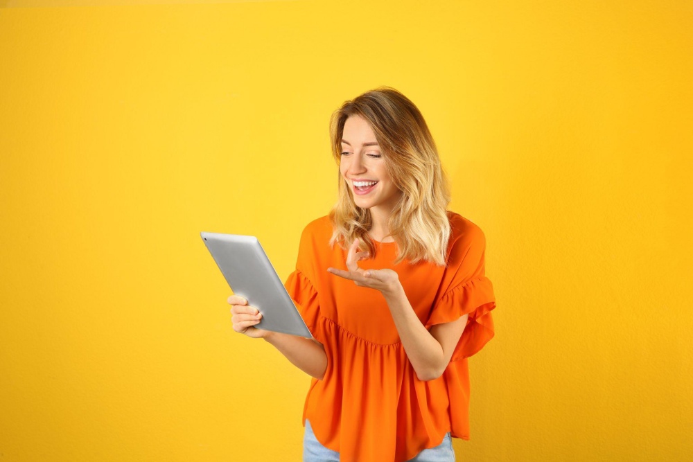 Smiling woman in orange using tablet with yellow background