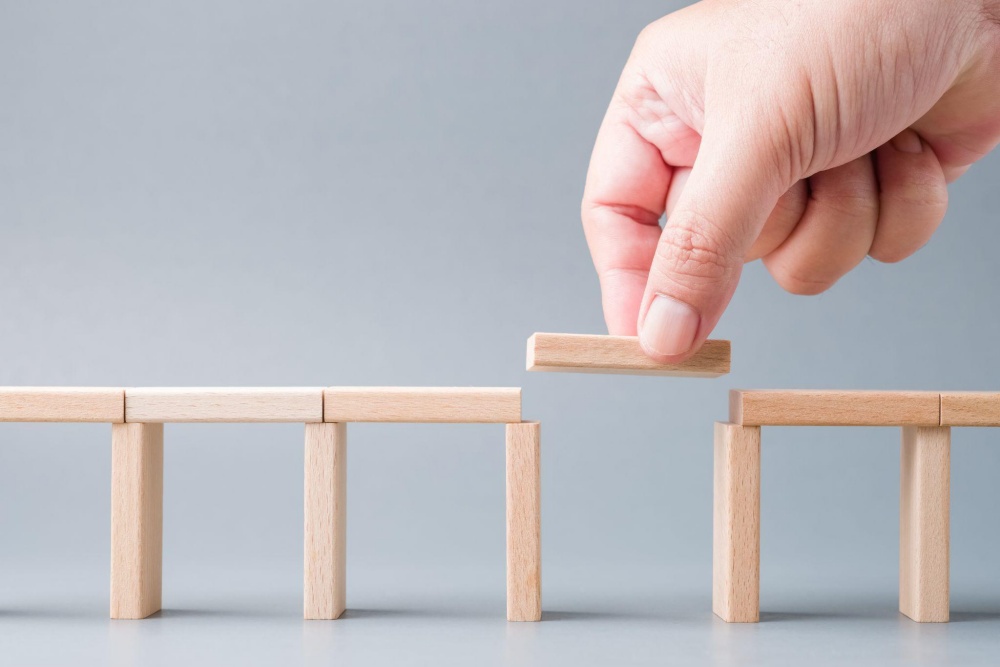 Hand placing wooden block to bridge gap in structure on gray background