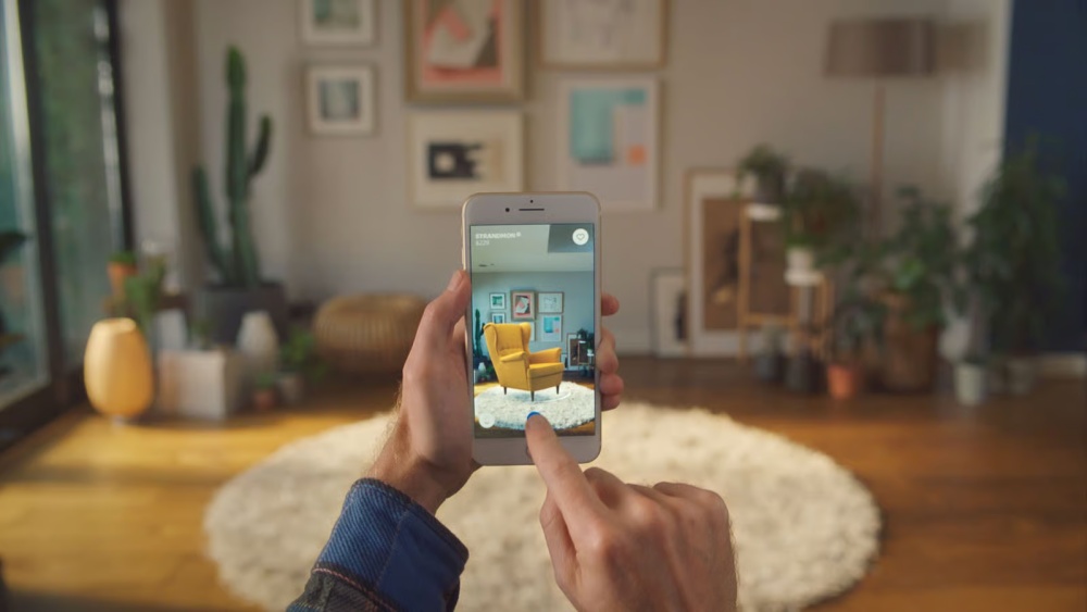 Hand using AR app on phone to visualize yellow chair in living room