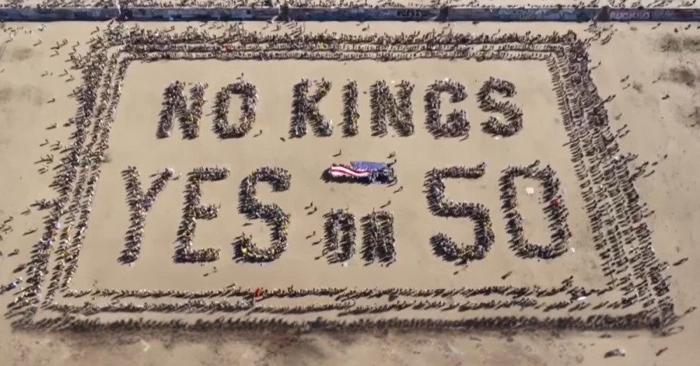 Aerial view of people forming 'No Kings Yes on 50' with an American flag on a beach