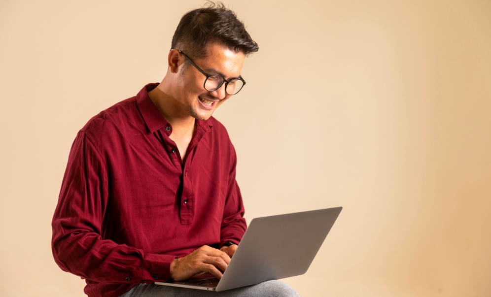 Man in maroon shirt typing on laptop, smiling.