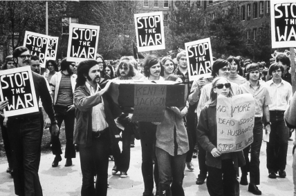 Protest with signs reading 'Stop the War' and 'Kent Jackson,' including 'No More Deads Stop the War