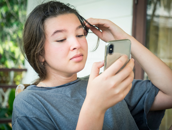 Young teen looking at her phone while playing with her hair.