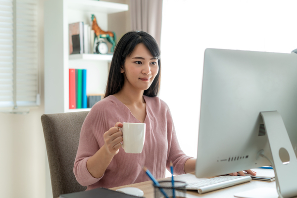 Woman looking at her desktop monitor while drinking a cup of coffee.