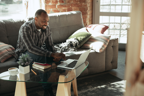 Smiling man sitting on a couch looking at his laptop screen.