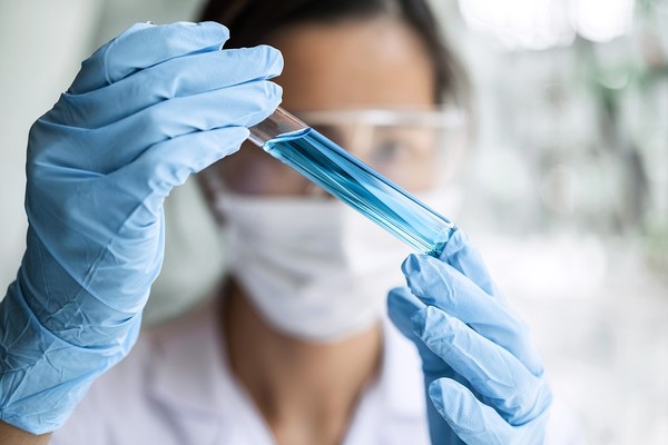 Woman holding a glass vial with a blue liquid.