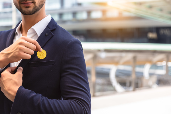 Business man placing a gold coin labeled with a bitcoin symbol in his pocket.