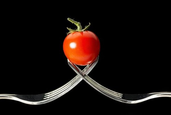 Two forks holding a cherry tomato.