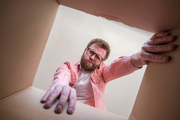 Man looking inside a cardboard box with a puzzled expression.