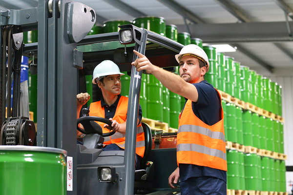 Workers with orange vests and green barrels in the background.