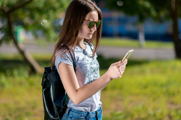 Woman standing outside with a backpack looking at her phone.