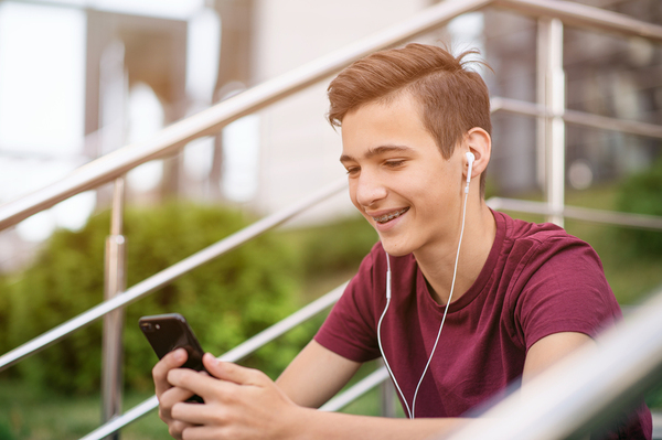 Young teen sitting on steps smiling while looking at his phone.
