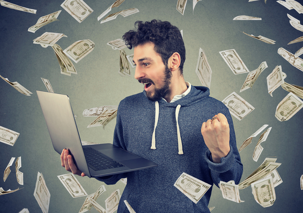 Man standing holding his laptop with cash falling down around him.