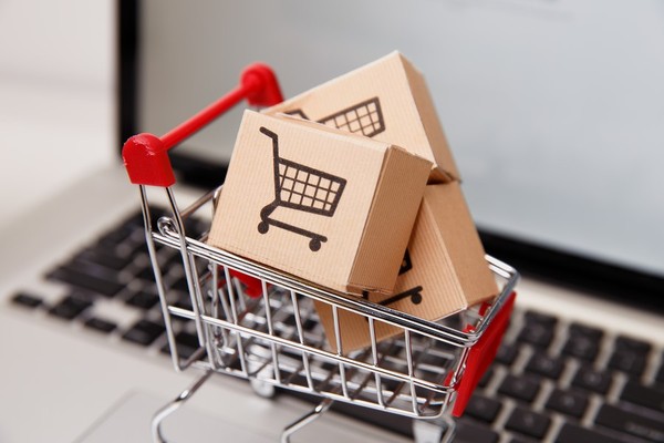 Miniature shopping cart with small cardboard boxes inside.