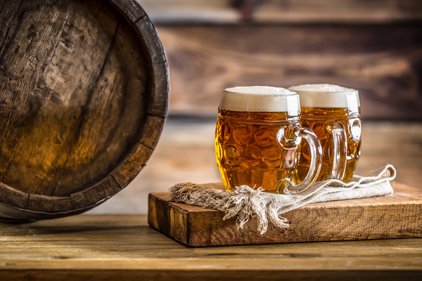 Two glasses of beer next to a wooden barrel