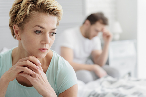 Woman looking down disappointed with man in the background with his hand on his forehead looking upset.