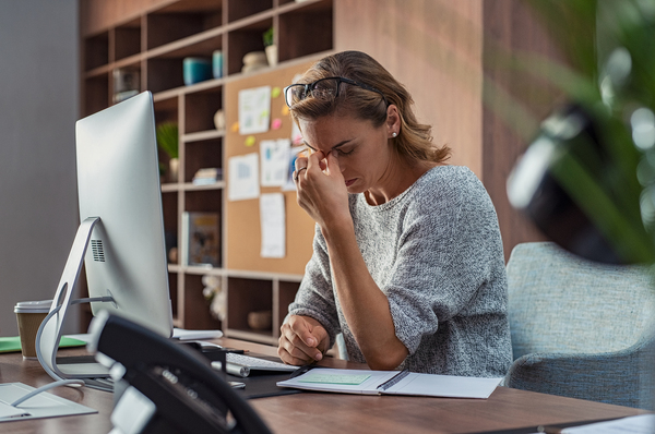 Woman sitting at her desk holding her head with her hand.