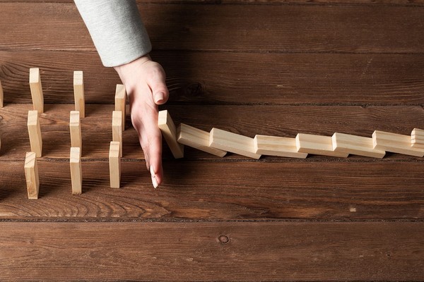 Dominos lined up to fall down, with a hand blocking some of them.