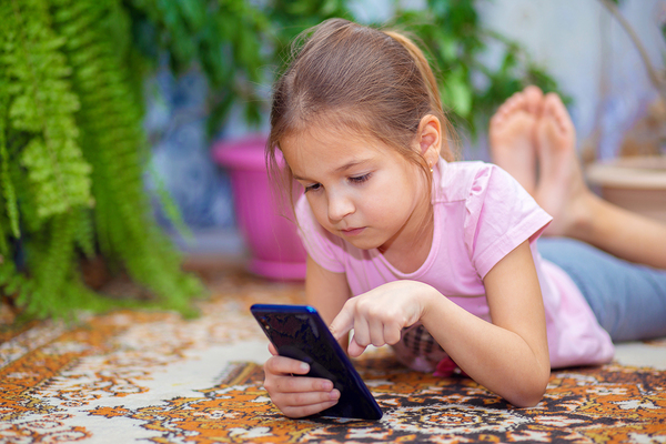 Young girl lying on the floor typing on a phone.