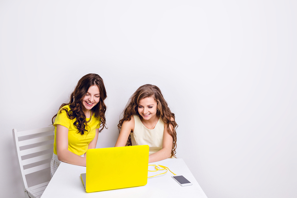 Two teens smiling while looking at a laptop screen.