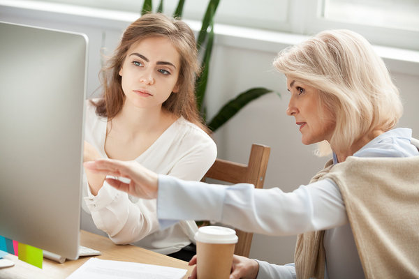 Two woman discussing work in front of a desktop computer.