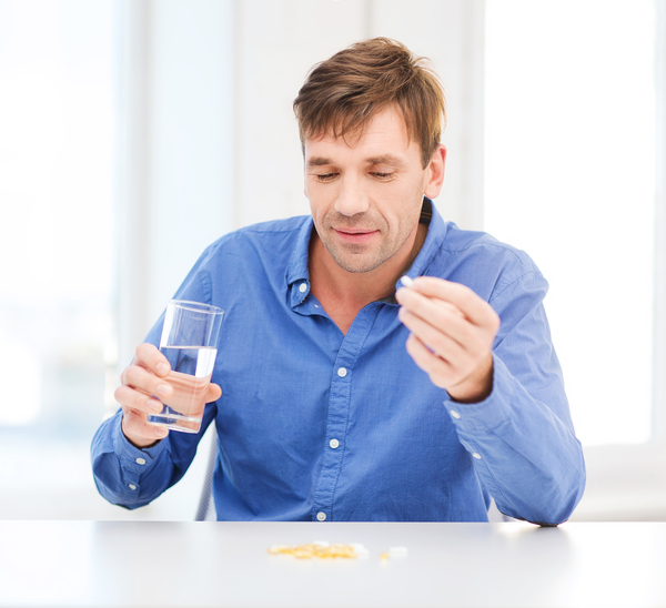 Man taking a pill with a glass of water.