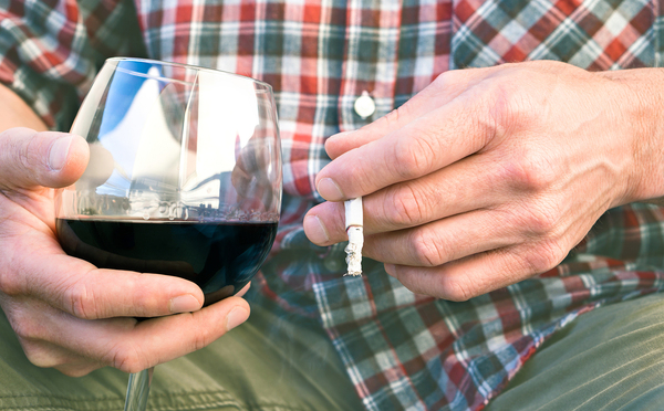 Man smoking a cigarette and drinking a glass of wine.
