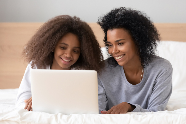 Mother and teen daughter smiling while looking at a laptop computer together.
