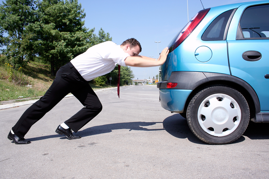 Man in dress clothes pushing blue car from
