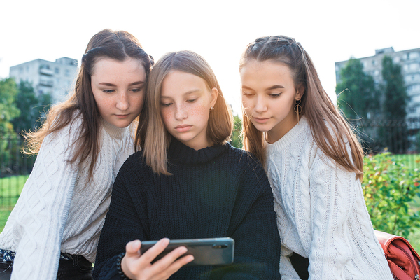 Three young teens looking at a phone together outside.