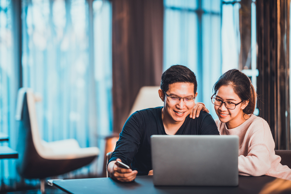 Two people sitting in front of a laptop computer smiling.