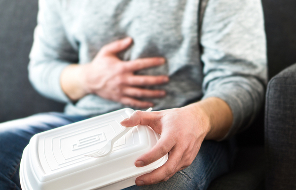 Person holding their stomach and styrofoam food container.