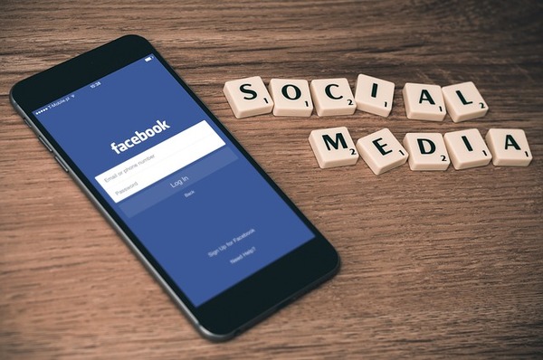 (Table with smartphone opened to Facebook and blocks spelling out social media.) There are many different channels for real-time marketing, but social media is one of the best thanks to its immediacy.