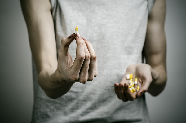 Person holding a pile of pills in one hand and holding up one pill in the other.