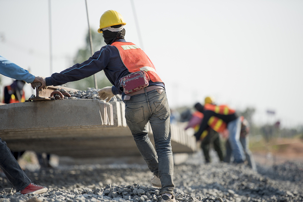 Construction workers assisting a crane with placement of concrete slab.