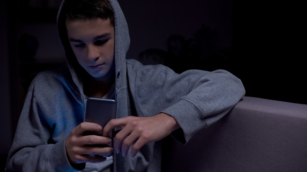 Teen sitting down looking at his phone screen.