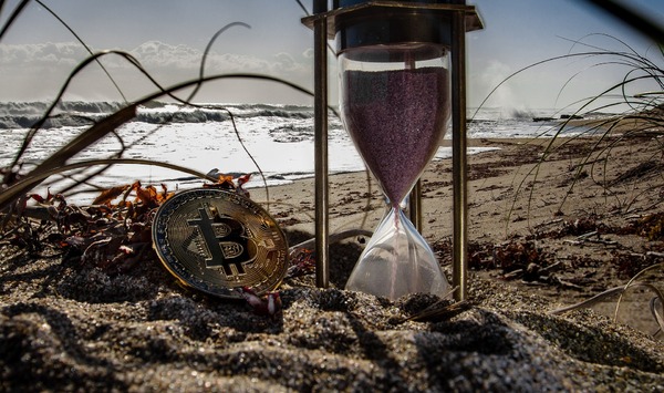 Hourglass on a beach with the gold bitcoin coin.