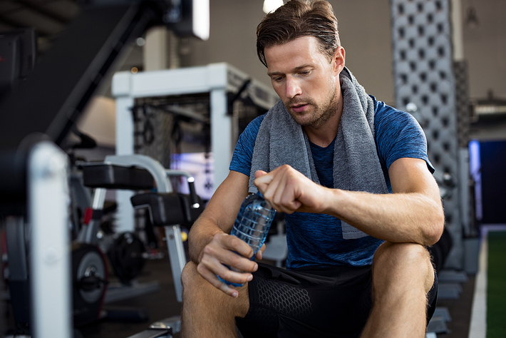 Man sitting in a gym opening a water bottle.