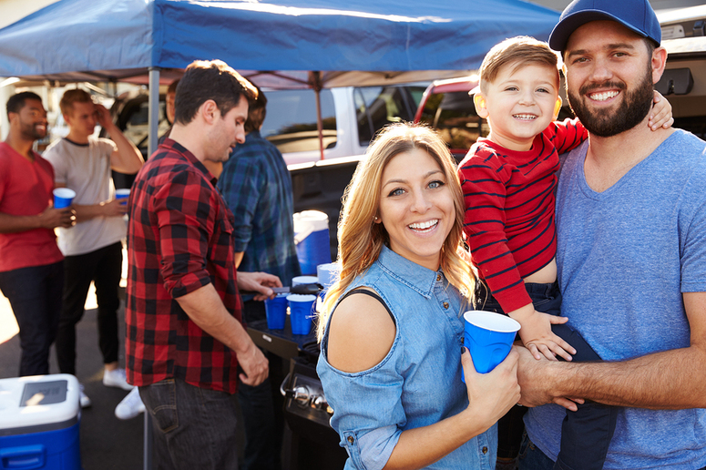 Family of two parents and one child outside smiling.