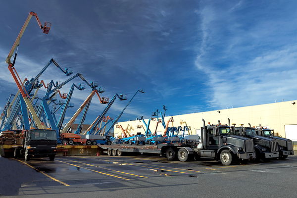 Several lifts on the back of flatbed trucks in a parking lot.