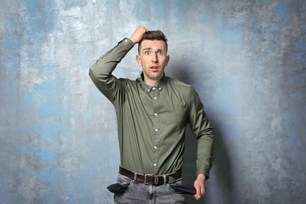 Man with empty pockets and his hand on his head in frustration.