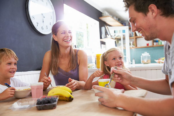 Family sitting down and eating breakfast smiling.